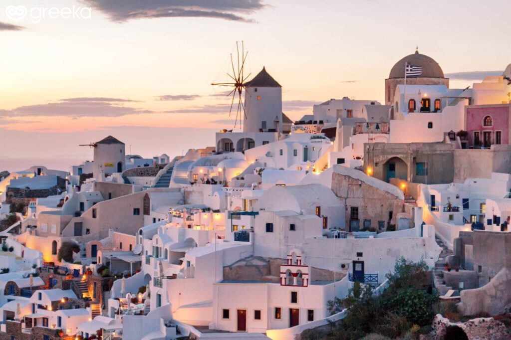Whitewashed houses and windmill in Oia Santorini at sunset with warm lights and pastel sky