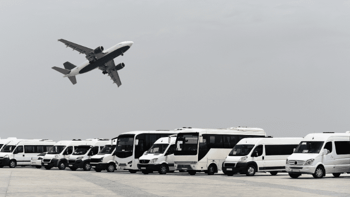 Plane taking off above a row of private vans and minibuses lined up for fast, stress-free Santorini airport transfer pickups