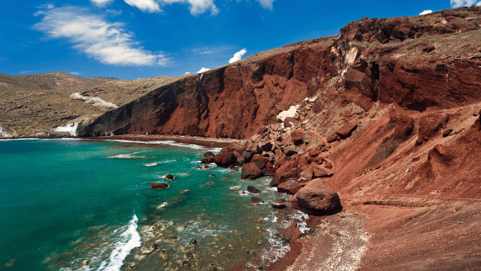 red beach view in Santorini with mild waves and a clear sky with minor clouds in October