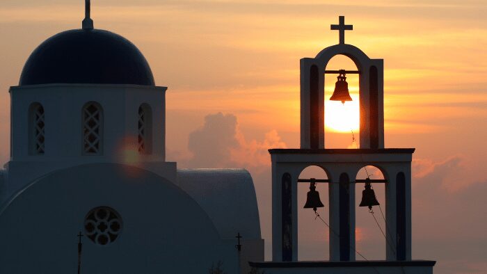 Santorini church with blue dome and bell tower at sunset in Oia, symbolizing the island’s iconic scenery for arriving travelers.