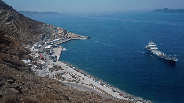 Scenic view of Santorini’s Athinios Port from above with ferry and port traffic visible, ideal for showcasing port logistics.