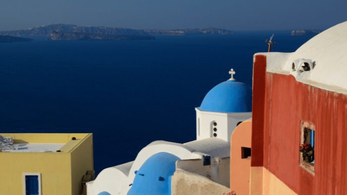 Blue-domed church and colorful buildings overlooking the Aegean Sea in Santorini.