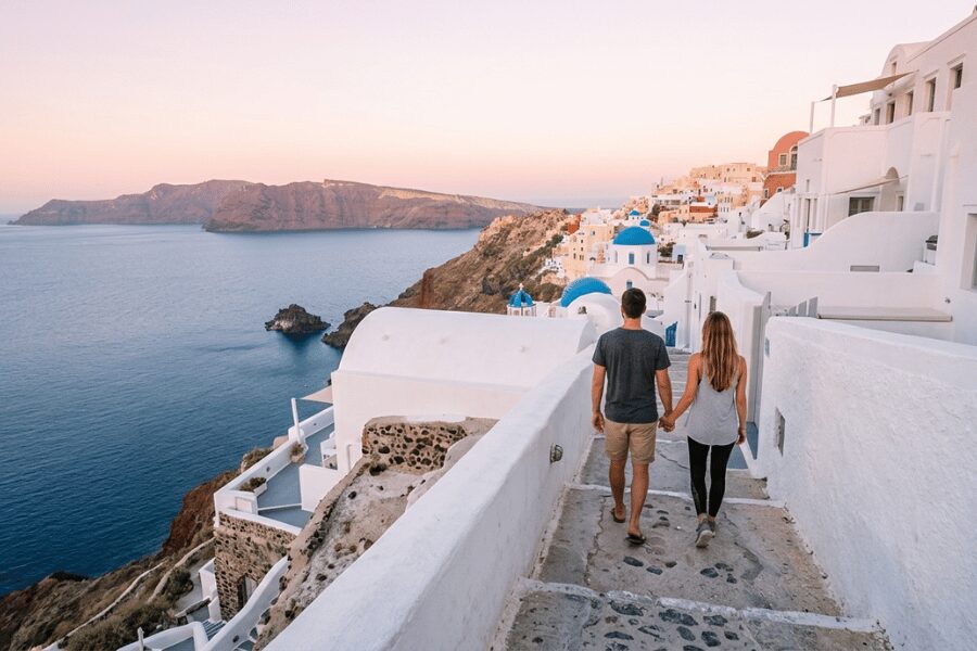 Couple walking caldera footpath between Fira and Oia Santorini at sunrise with whitewashed walls and volcanic sea views