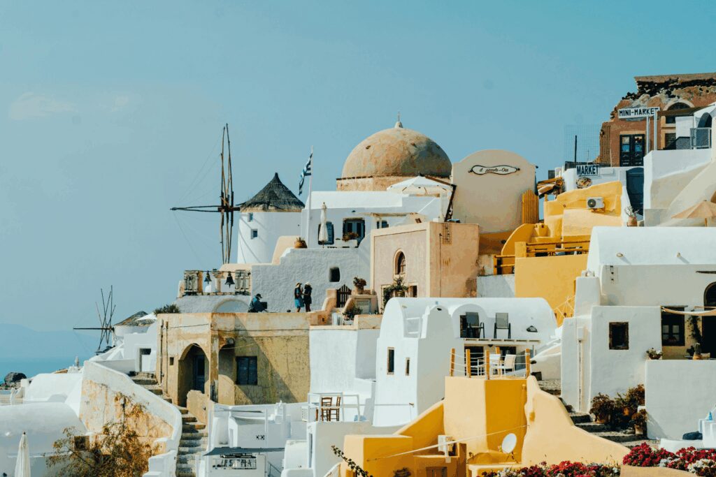 Traditional windmill and whitewashed buildings with golden domes in Fira Santorini under a clear blue sky