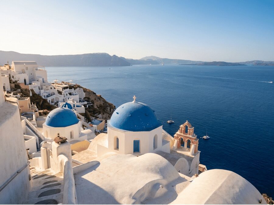 Blue-domed churches and whitewashed houses of Oia village Santorini cascading toward the Aegean Sea
