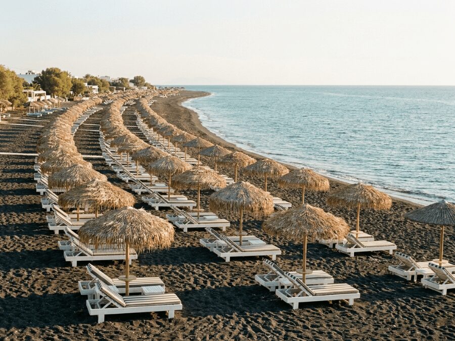 Black sand beach at Perivolos Santorini with sunbeds, umbrellas, and calm Aegean Sea in summer